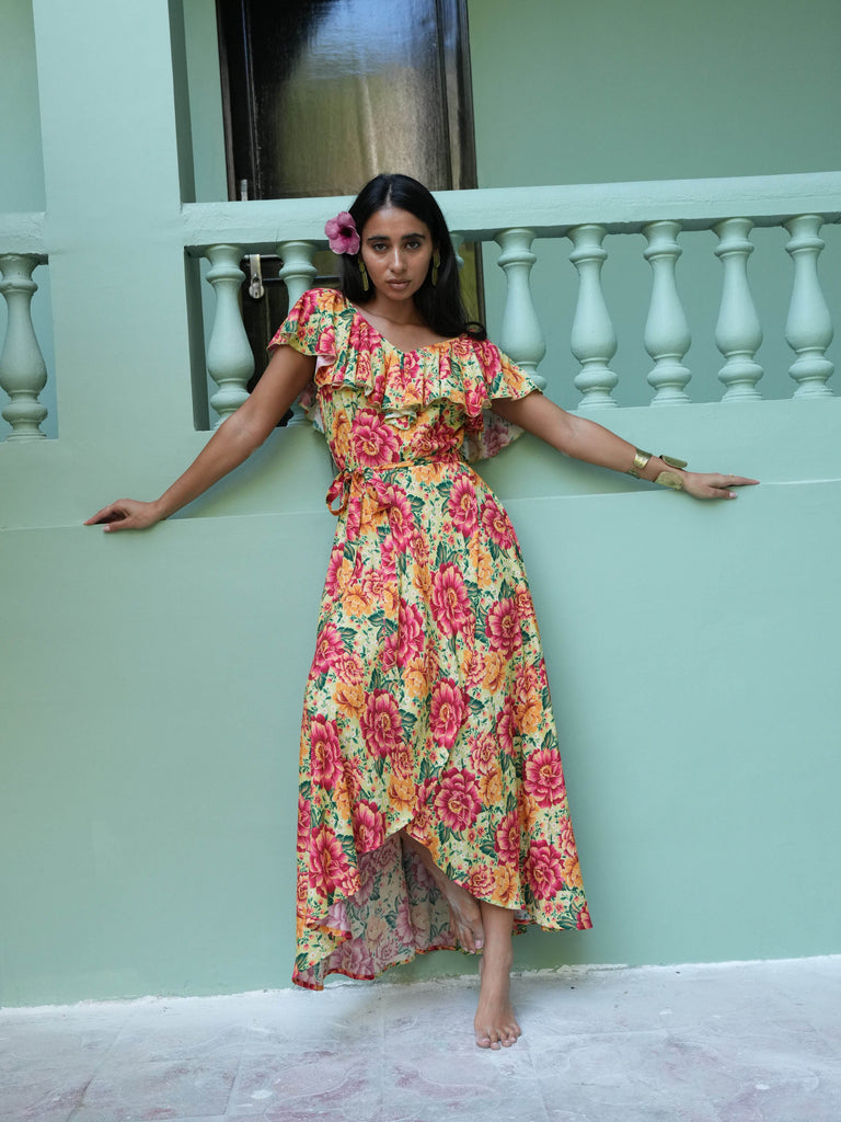 Woman in a floral dress standing against a light green wall.