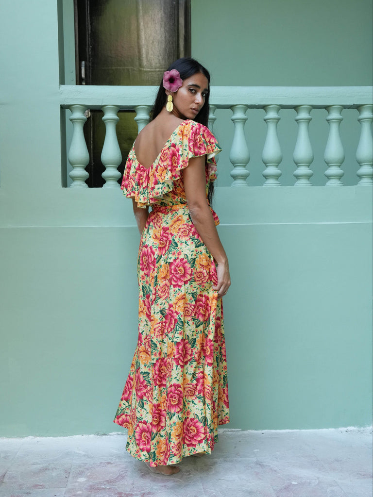 Woman in a colorful floral dress standing against a light green wall.