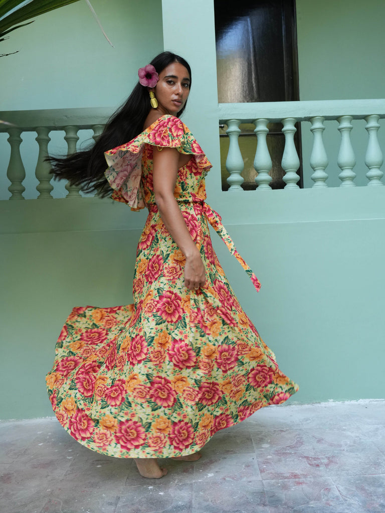 Woman in a colorful floral dress standing in front of light green wall and railing.