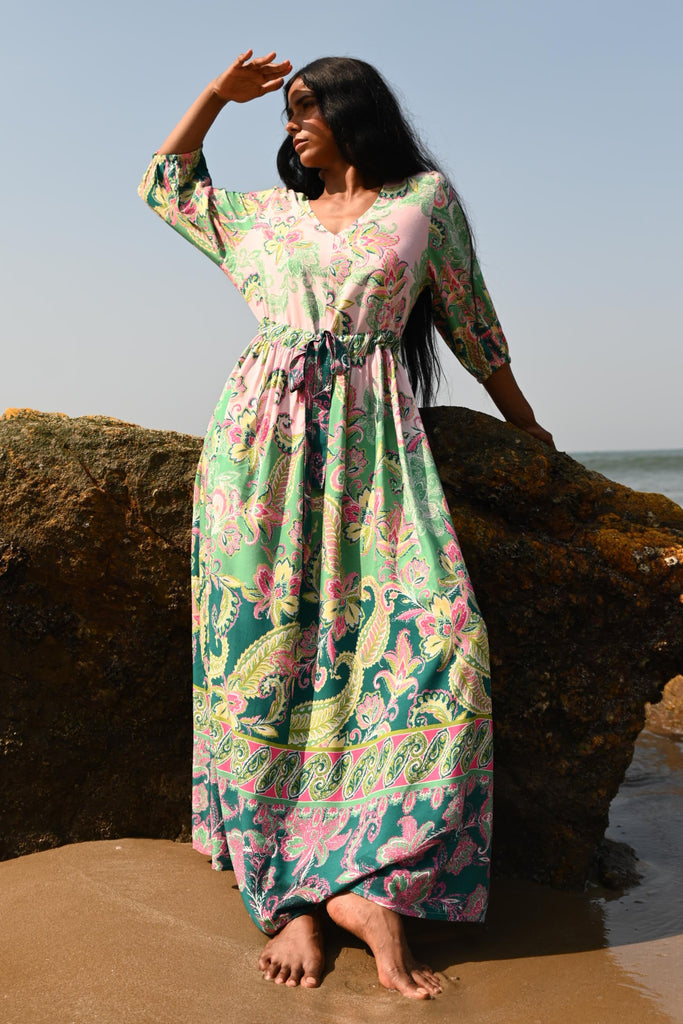 Person in a floral dress standing on a rock with a clear blue sky background