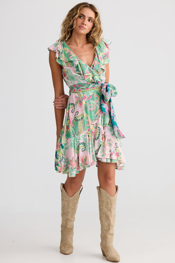 Woman wearing a floral dress with ruffled neckline and hem, paired with beige knee-high boots on a white background.