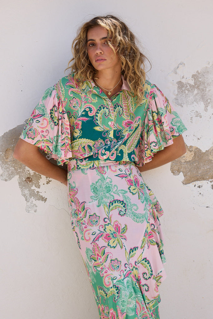 Woman wearing a colorful floral outfit against a textured wall.