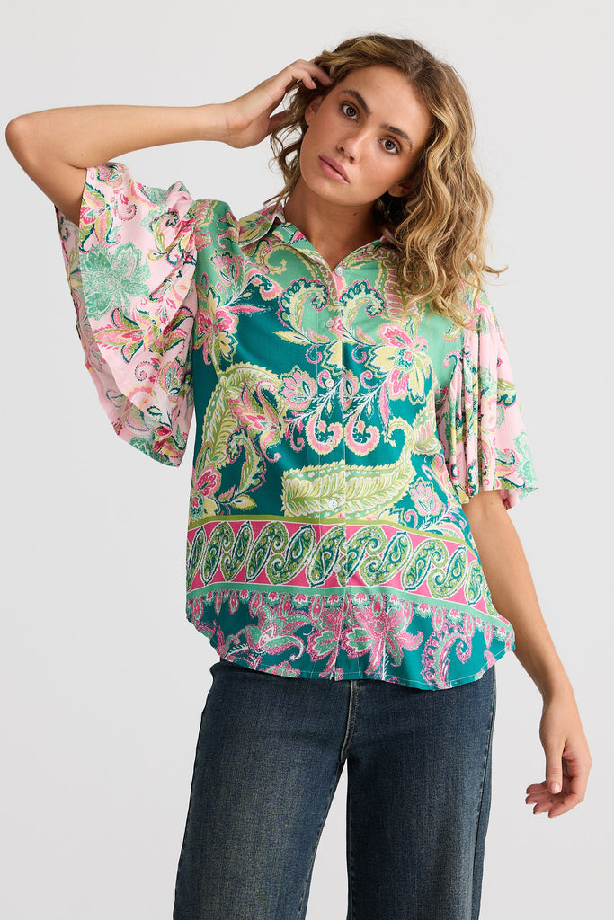 Woman wearing a colorful patterned blouse with bell sleeves on a white background