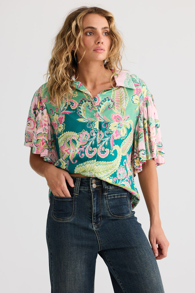 Woman wearing a colorful patterned blouse and jeans on a white background
