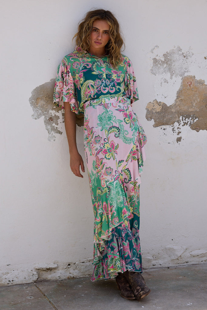 Woman wearing a floral dress standing against a white wall with peeling paint.