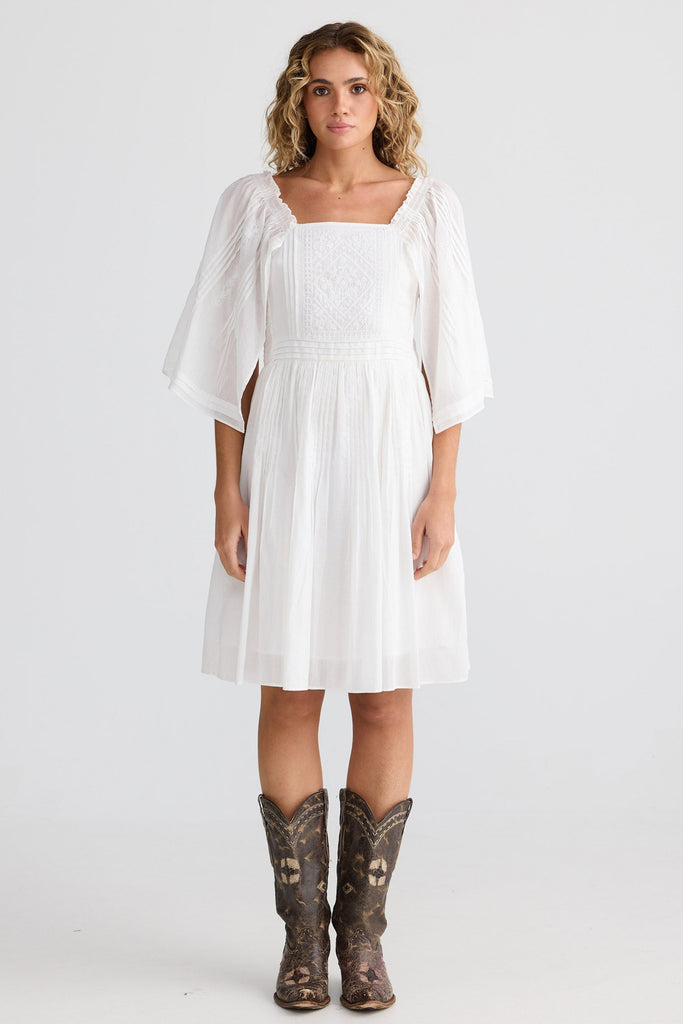 Woman wearing a white dress and cowboy boots on a plain background