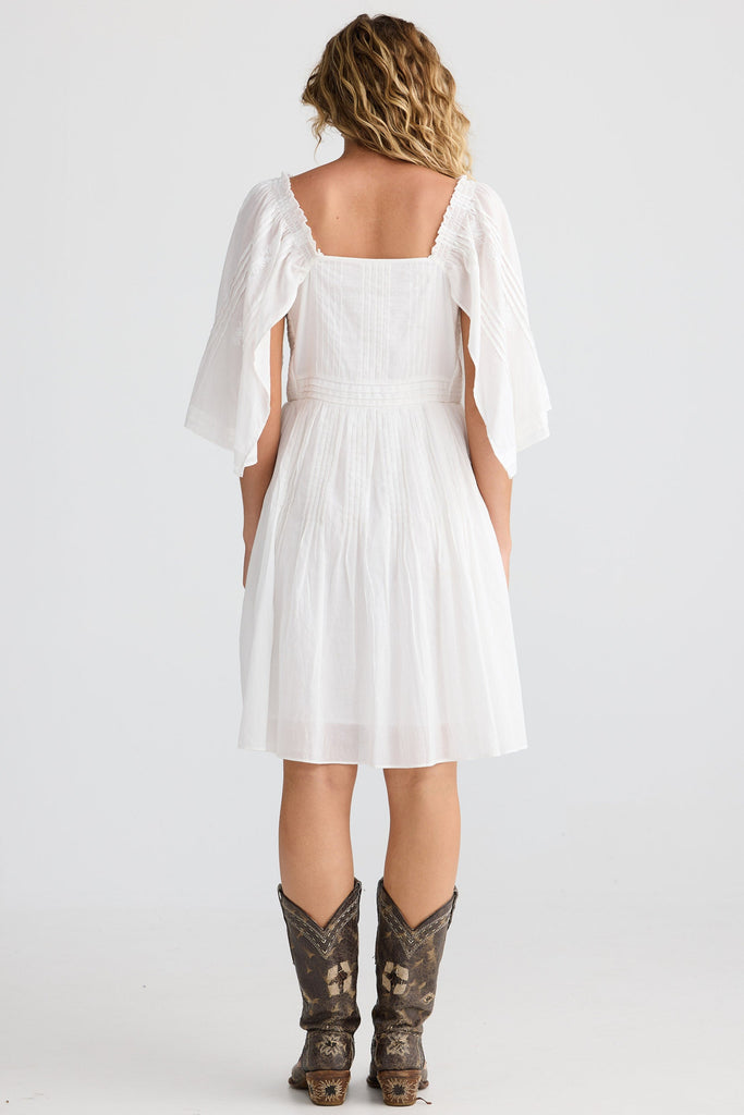 Woman wearing a white dress with sleeves and cowboy boots on a white background