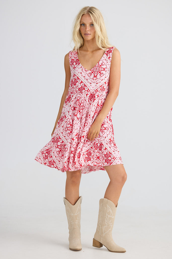 Woman wearing a red patterned dress  and beige cowboy boots on a white background