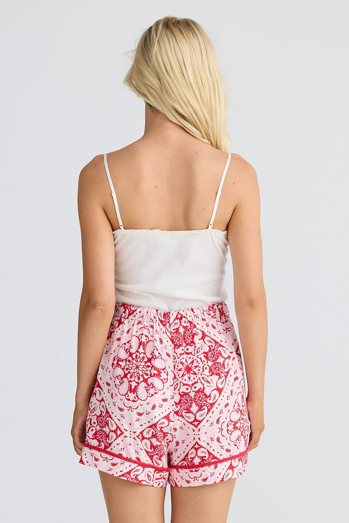 Person wearing a white top and red patterned shorts on a white background