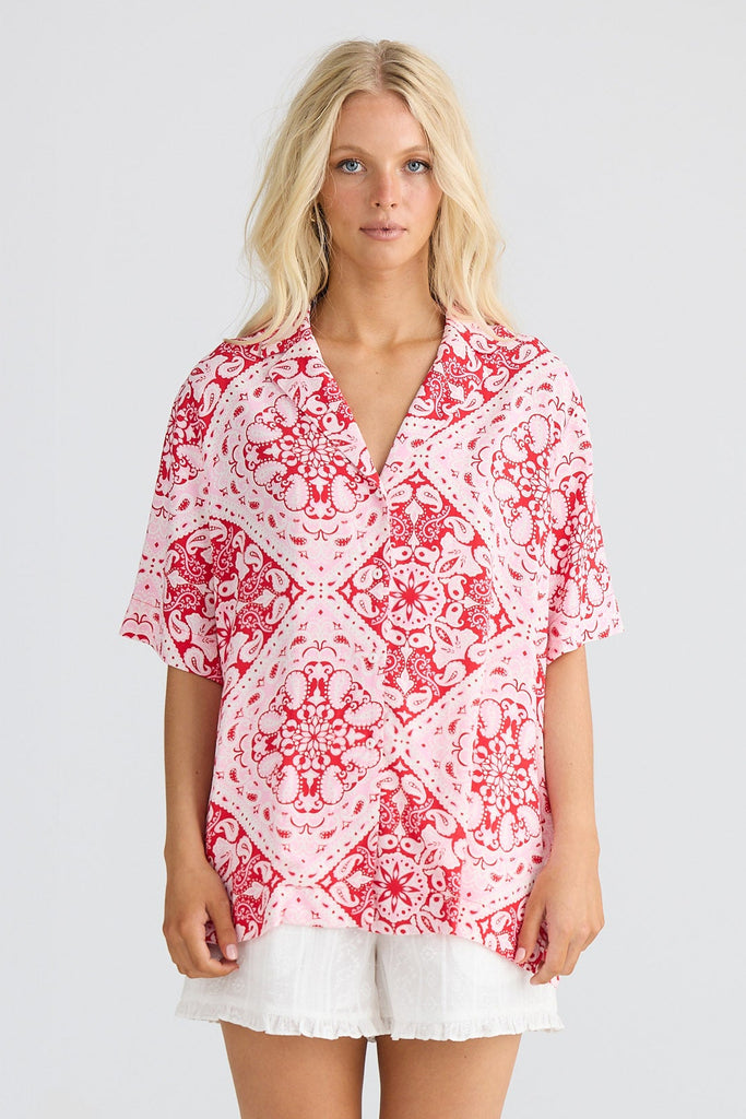 Woman wearing a red patterned shirt with white shorts on a white background