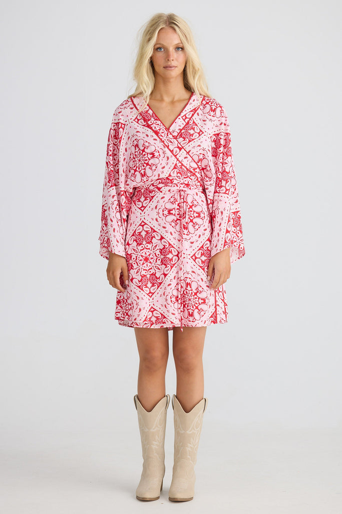 Woman wearing a red and white patterned dress with beige cowboy boots on a white background