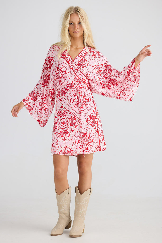 Woman wearing a red and white patterned dress with beige boots on a white background