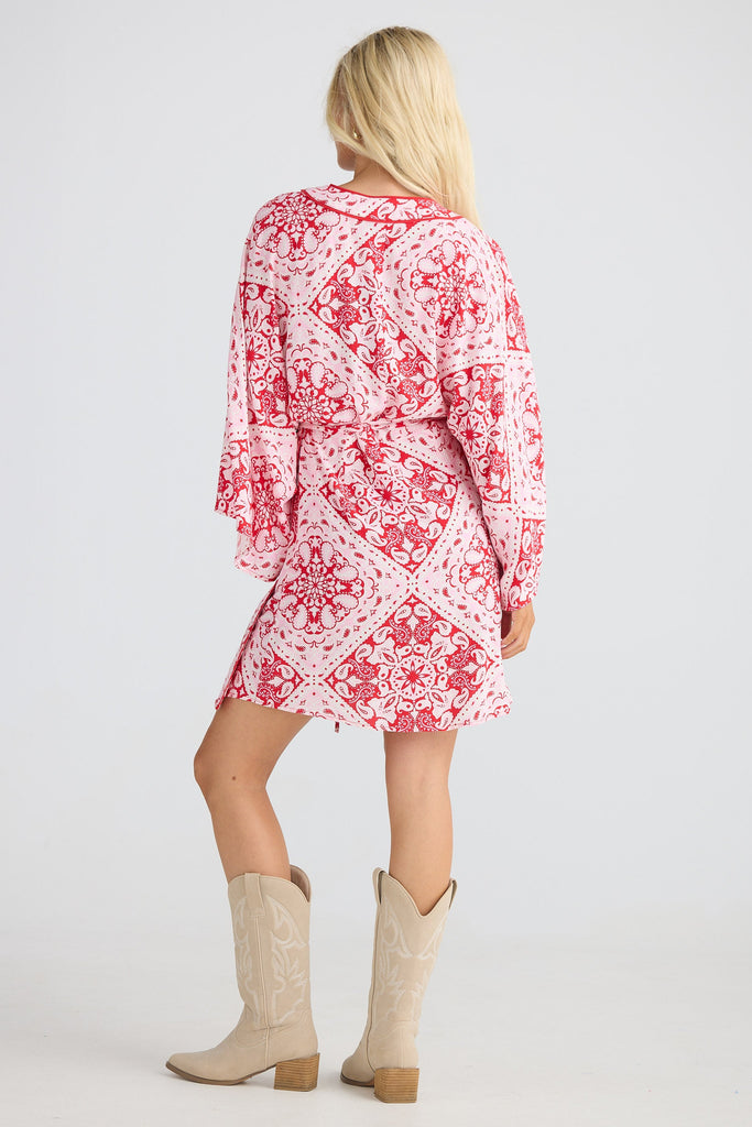 Woman wearing a red and white patterned dress with beige boots on a white background