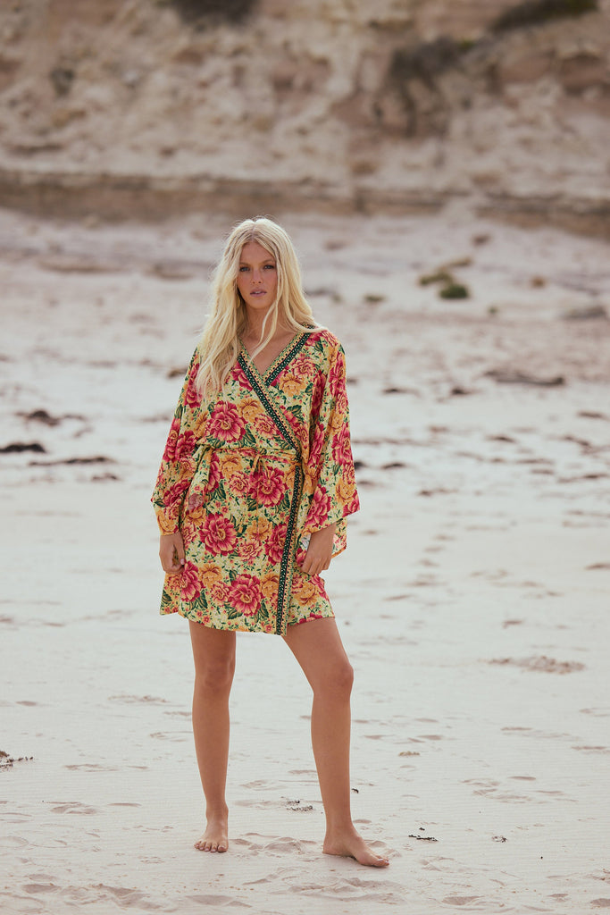 Woman in a floral dress standing on a sandy beach.