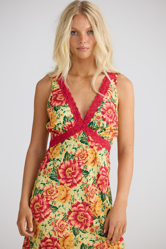 Woman wearing a colorful floral dress with a red lace overlay on a white background