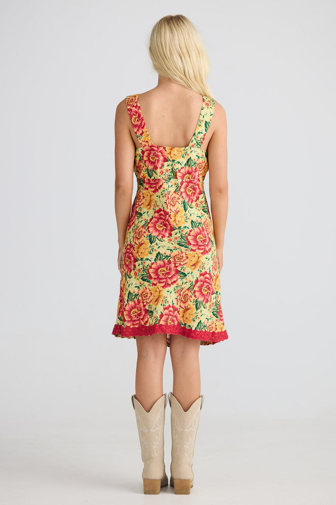 Woman wearing a floral dress with red trim and beige cowboy boots on a white background