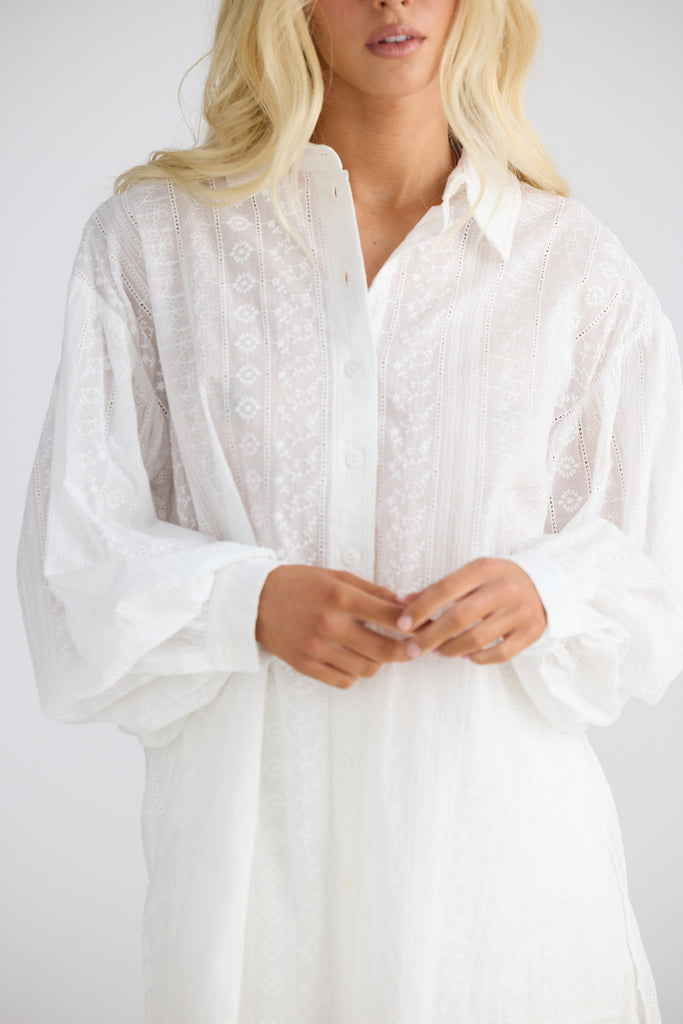 Person wearing a white lace shirt against a plain background