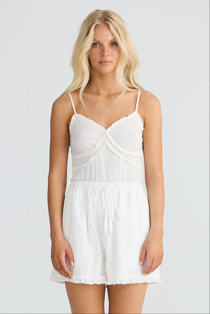 Woman wearing a white singlet and shorts on a plain background