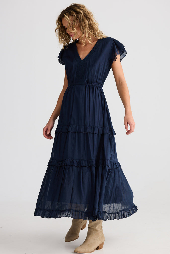 Woman wearing a navy blue dress with ruffled sleeves and tiered skirt on a white background