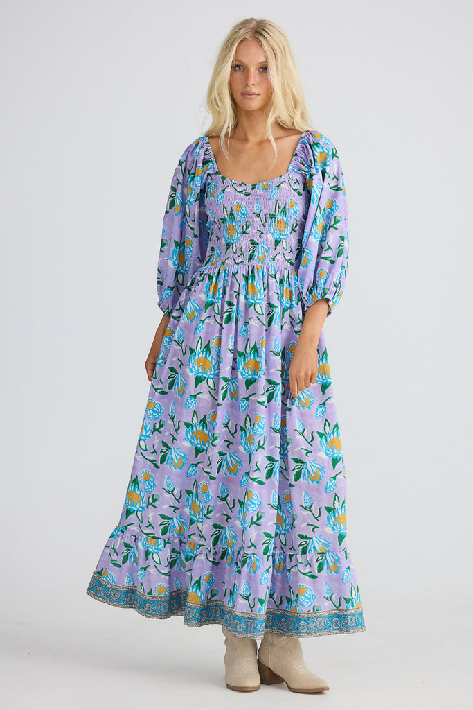 Woman wearing a long floral dress with a plain background