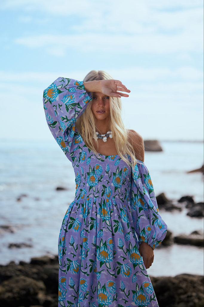 Woman in a floral dress standing on a beach with ocean in the background