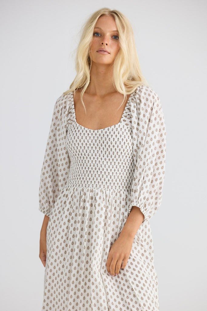 Woman wearing a long, patterned dress against a plain background