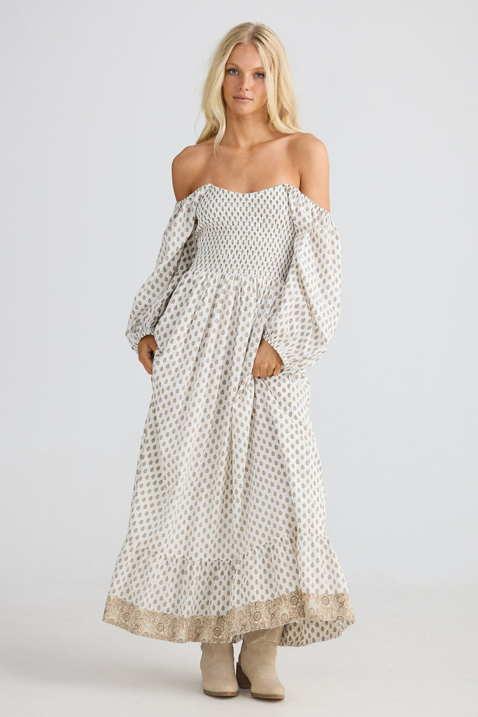 Woman wearing a long, patterned dress with long sleeves on a white background