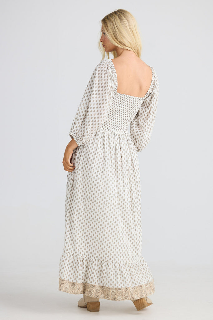 Woman wearing a long, patterned dress on a plain background