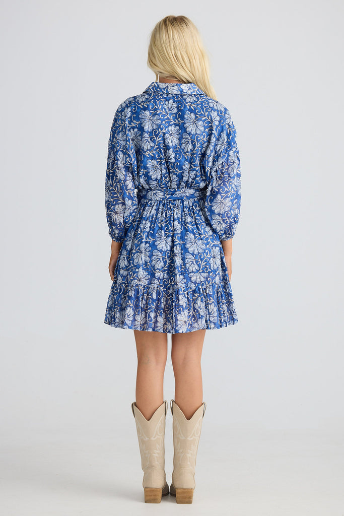 Person wearing a blue floral dress with beige boots on a white background