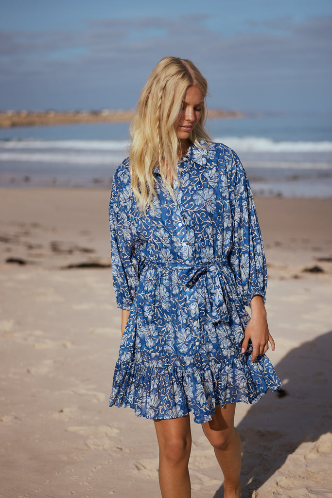 Woman in a blue floral dress standing on a beach