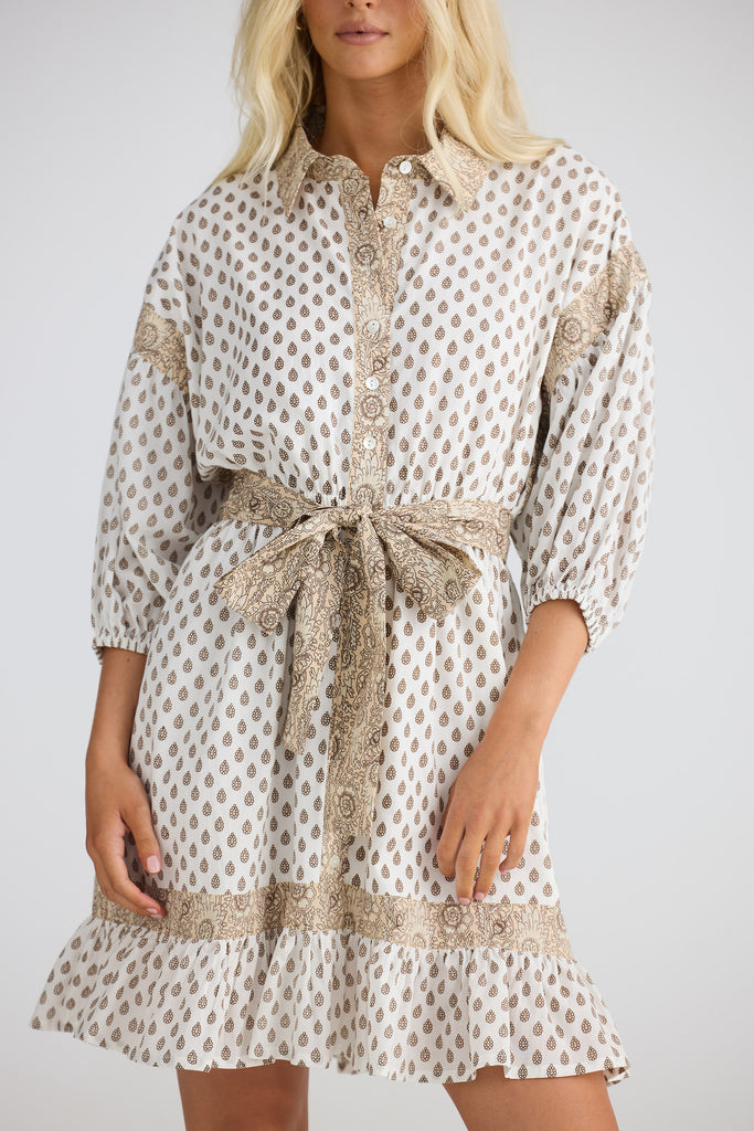 Woman wearing a patterned dress with a belt on a plain background