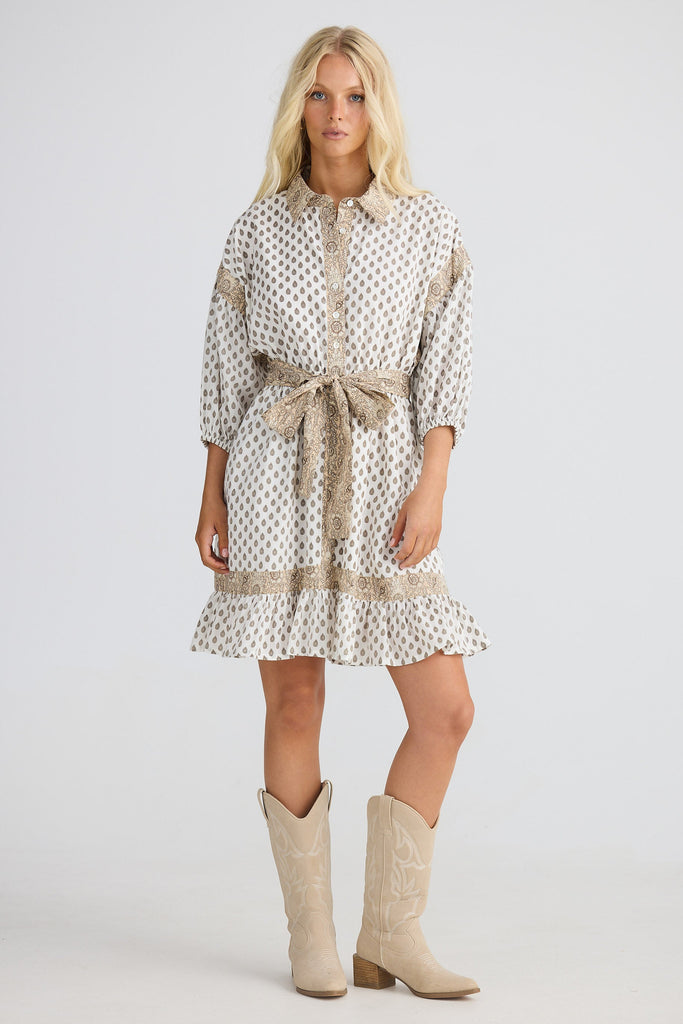 Woman wearing a patterned dress with a belt and beige boots on a white background