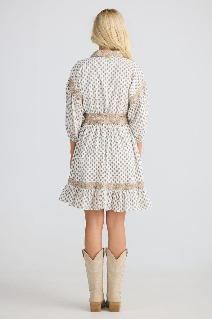 Woman wearing a patterned dress with a belt and beige cowboy boots on a white background