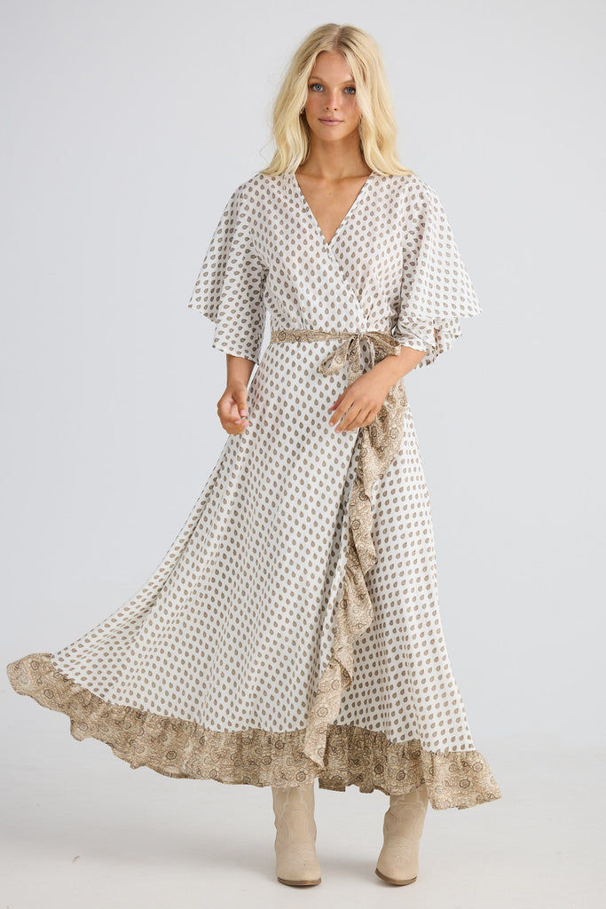 Woman wearing a long, patterned dress with a belt on a light gray background