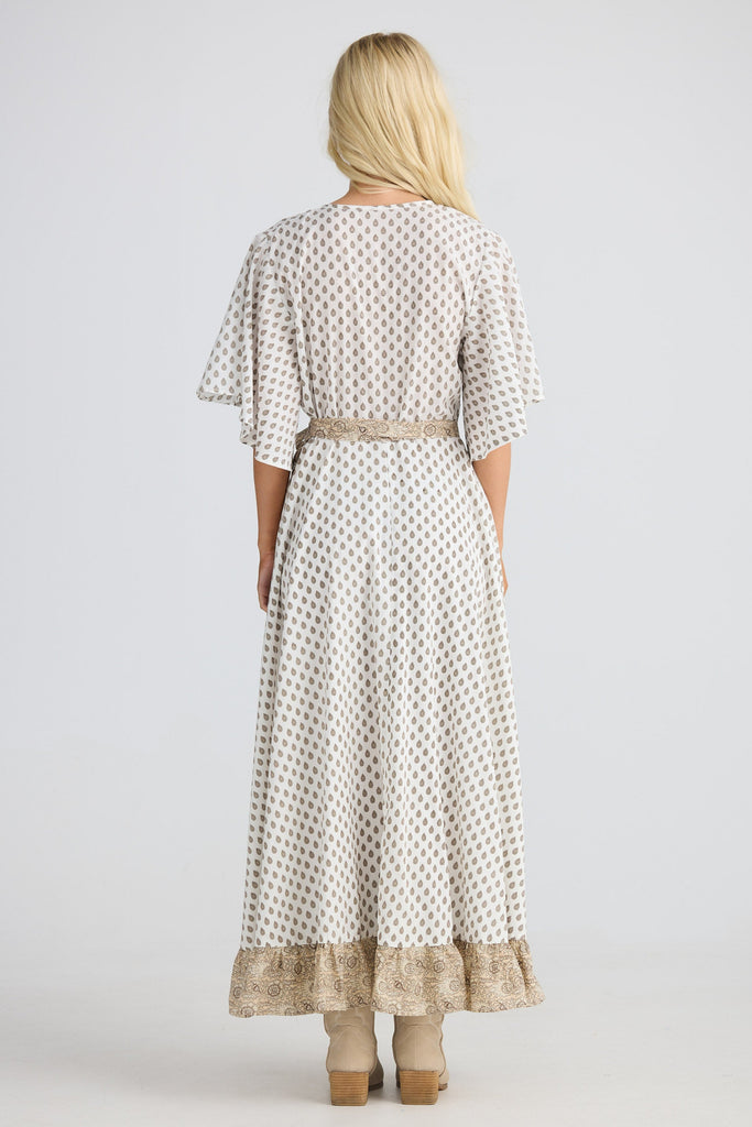 Woman wearing a long, patterned dress with a belt on a white background