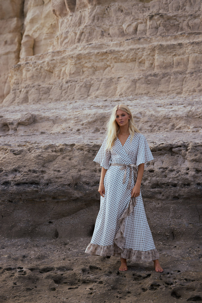 Woman in a patterned dress standing in front of a rocky cliff.