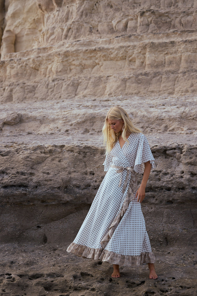 Woman in a patterned dress standing in front of a rocky wall.