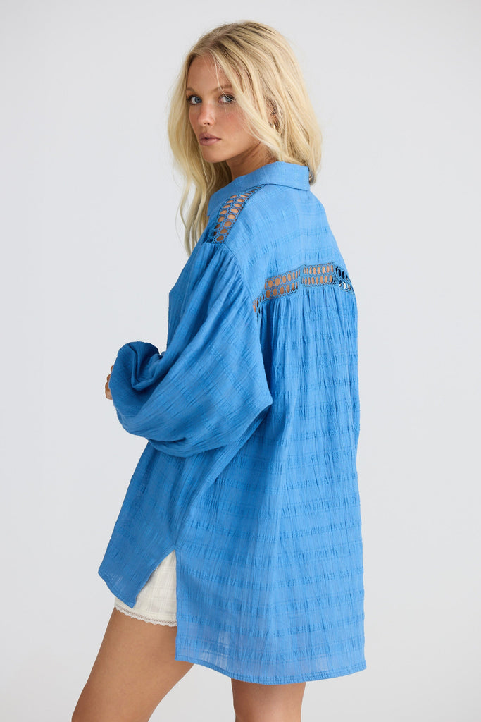 Woman wearing a blue shirt with lace details on a white background