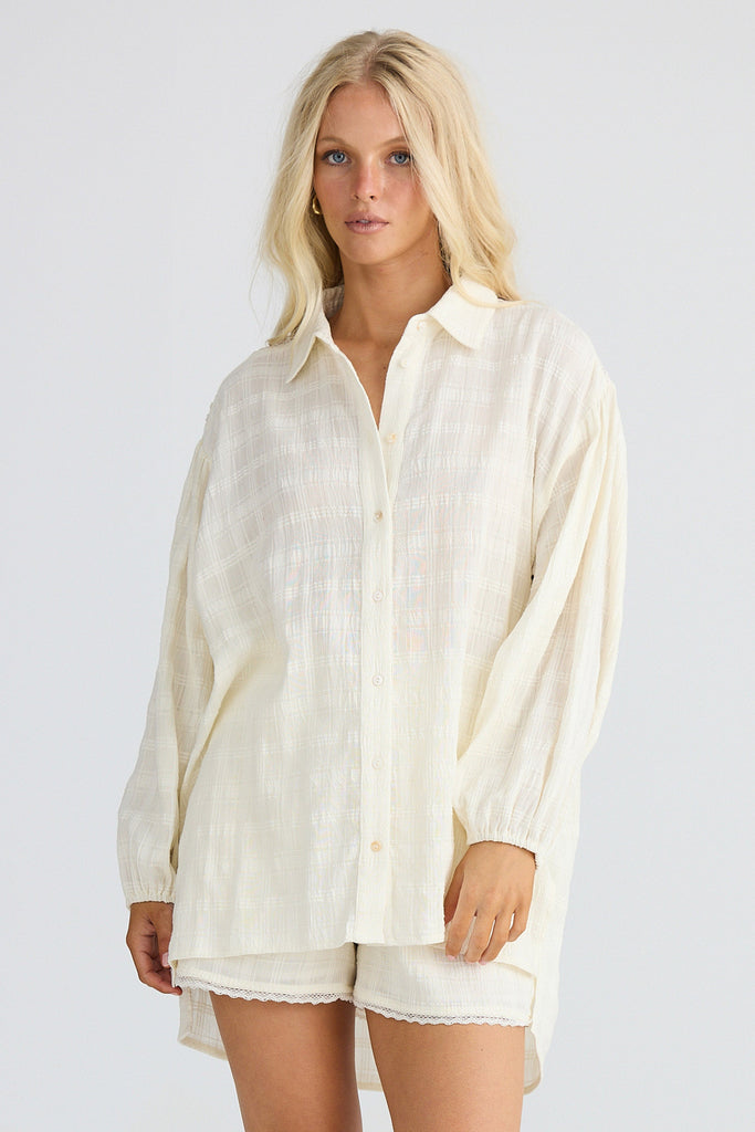 Woman wearing a cream button-up shirt and shorts on a plain background
