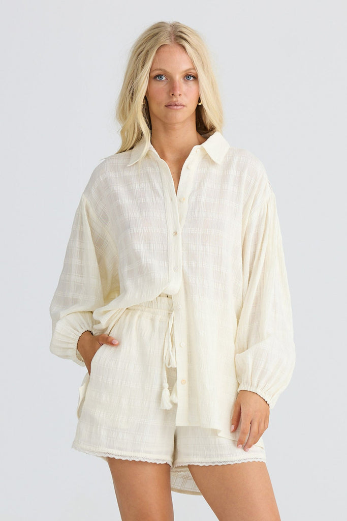 Woman wearing cream shirt and shorts on a plain background