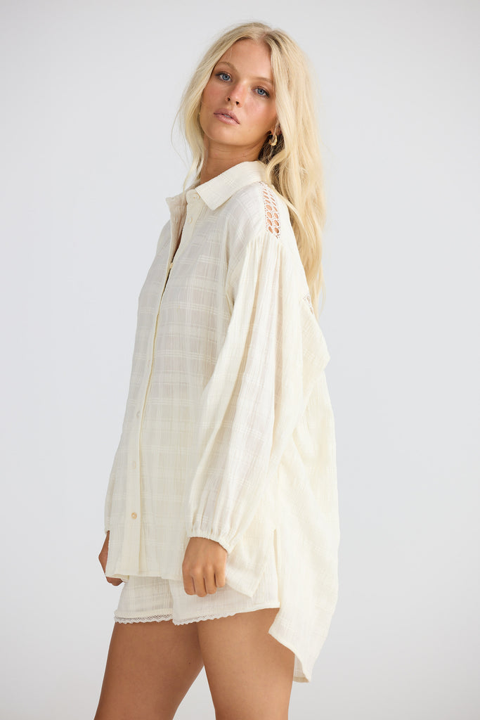 Woman wearing a cream coloured shirt and shorts with a plain background