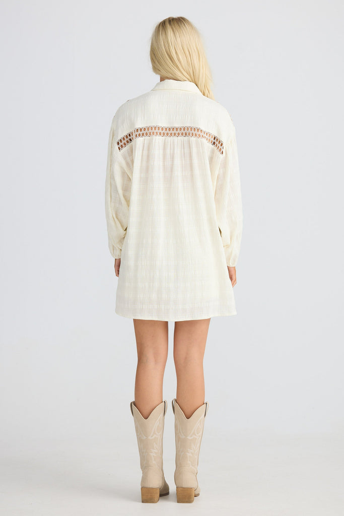 Person wearing a cream-colored long shirt with lace details and beige cowboy boots on a white background