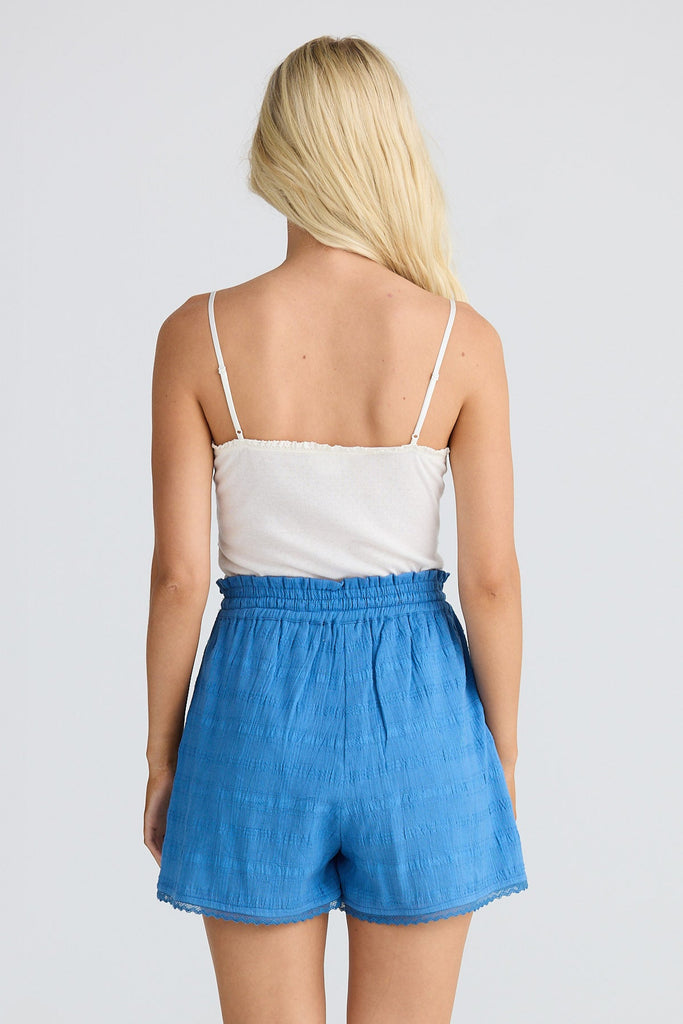 Person wearing a white top and blue shorts on a plain background