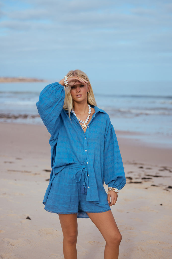 Woman in a blue outfit standing on a beach with ocean in the background