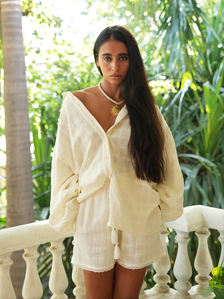 Woman in a white outfit standing on a balcony with greenery in the background