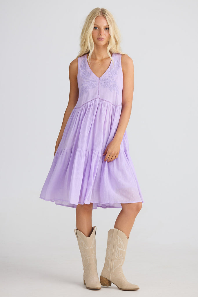 Woman wearing purple sleeveless dress with beige cowboy boots on white background