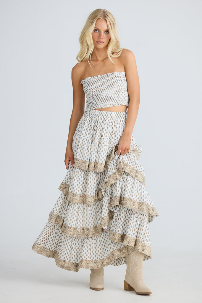 Woman wearing a white strapless top and ruffled skirt with beige accents on a light gray background