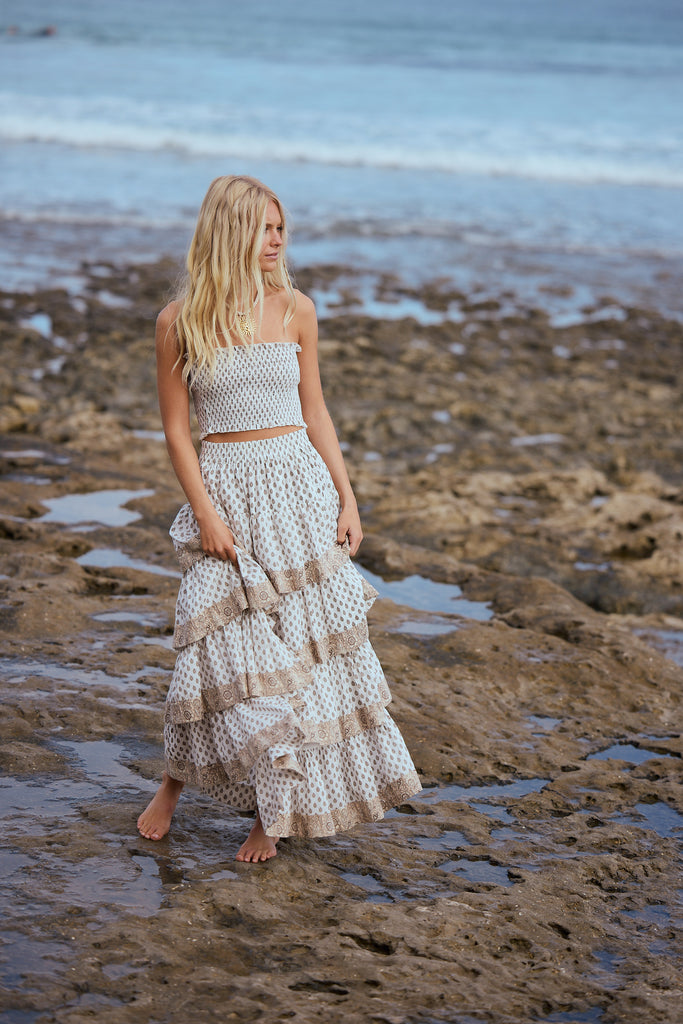 Woman in a layered skirt and strapless top standing on a rocky beach