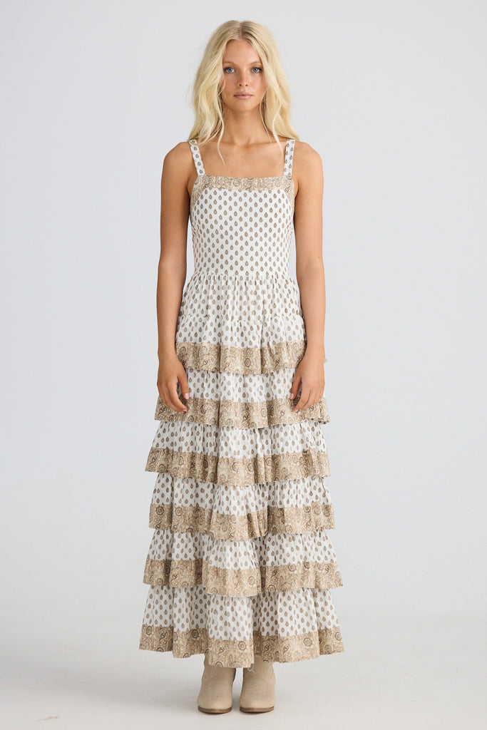 Woman wearing a tiered dress with white and beige pattern on a plain background