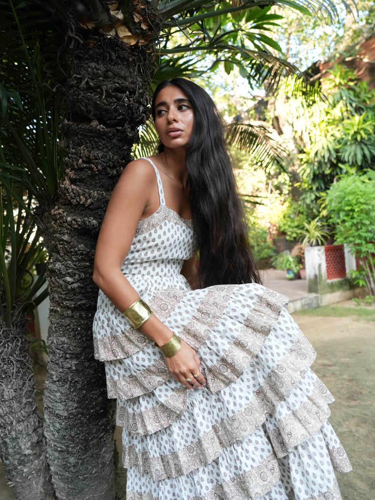 Woman in a white patterned dress standing next to a tree in a garden setting